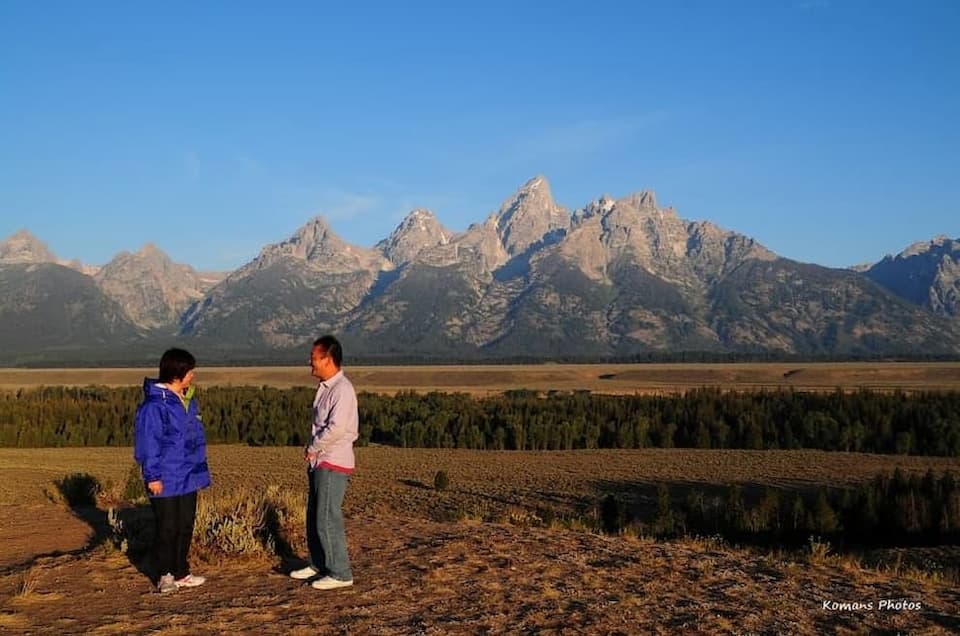 早朝の朝日に照らされるグランドティトン山脈の山並みをバックに記念撮影する２人