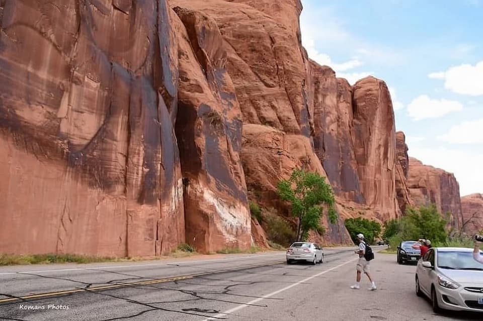 赤茶色の砂岩壁に描かれた先住民の岩絵を見行くため道路を横断しようとする人たち