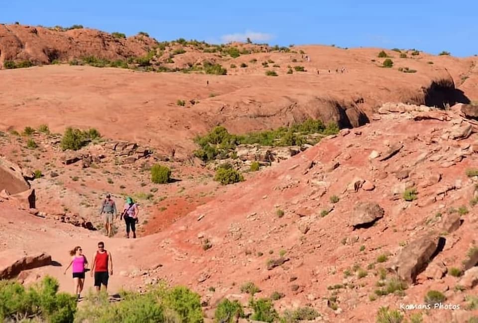快晴のもと赤茶色をした砂岩のハイキングトレイルを下ってくるハイカーと上方に豆粒のように見えるハイカーたち
