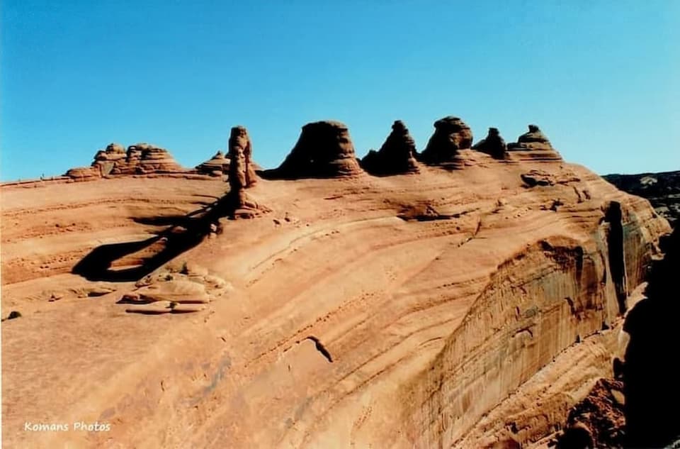 右奥から朝日にたらされる赤茶色の砂岩丘の上に立つデリケートアーチと左側に落ちる影